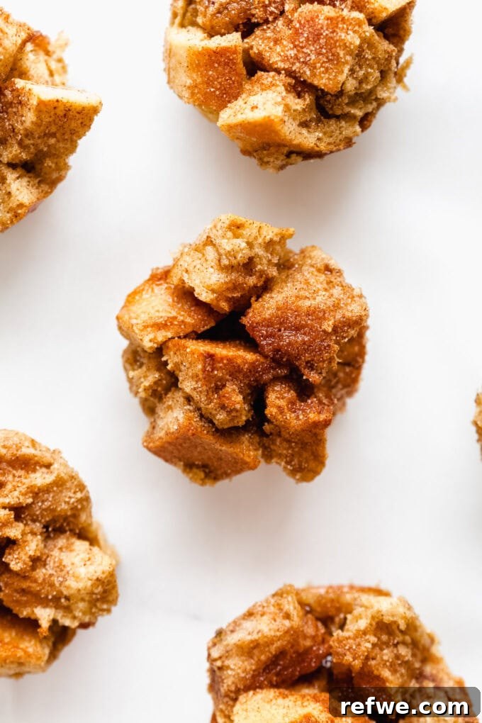 Golden brown French toast muffins arranged beautifully on a white marble board, some topped with a light dusting of cinnamon sugar.
