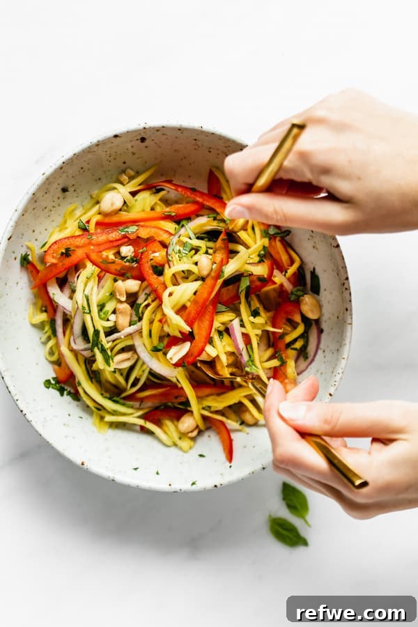 Zesty Thai Mango Salad 4 Two hands gently tossing a large bowl of colorful mango salad