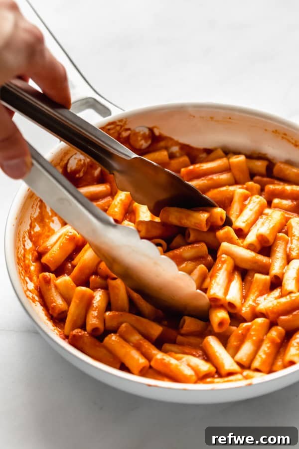 Velvety Vegan Roasted Red Pepper Pasta 4 Tongs gracefully scooping creamy roasted red pepper pasta from a pan, ready to serve.