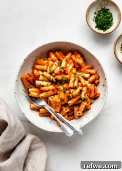 Creamy Vegan Roasted Red Pepper Pasta in a white speckled pasta bowl with a side of fresh parsley.