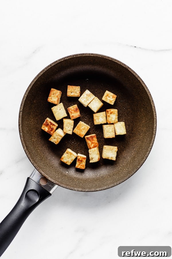 Crispy tofu cubes frying in a pan, achieving a golden-brown exterior.