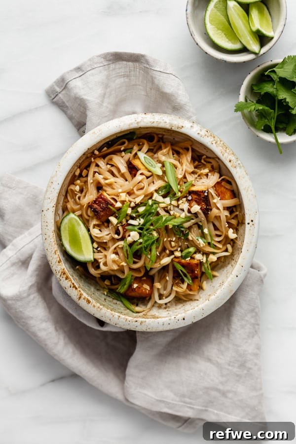 A beautifully plated bowl of vegan Pad Thai with tofu, garnished with cilantro and served on a grey napkin.