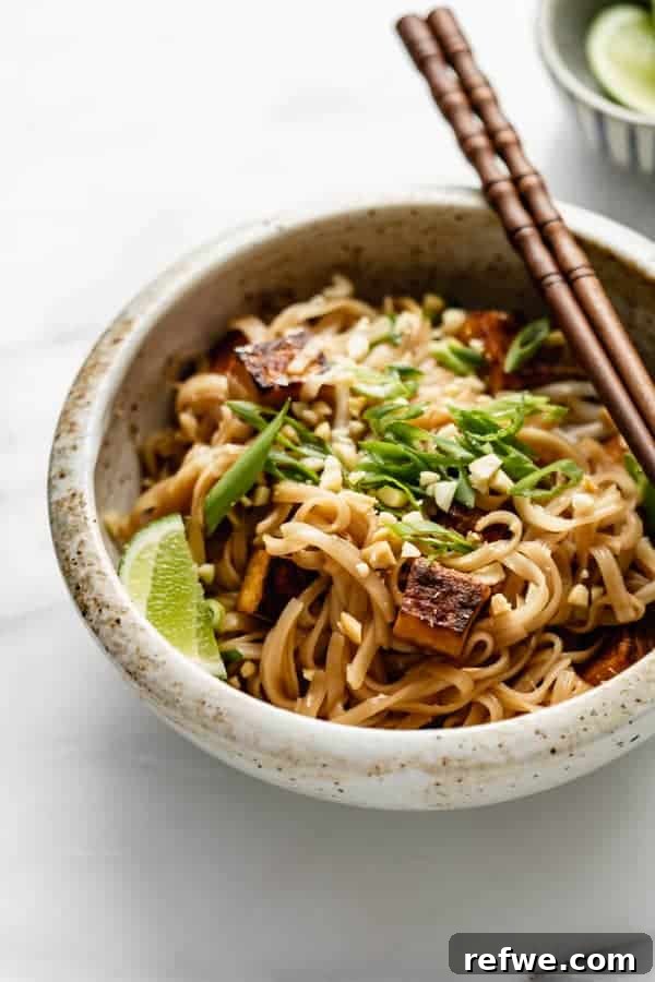 A bowl of vibrant vegan Pad Thai, garnished with fresh scallions and a lime wedge, ready to be enjoyed.