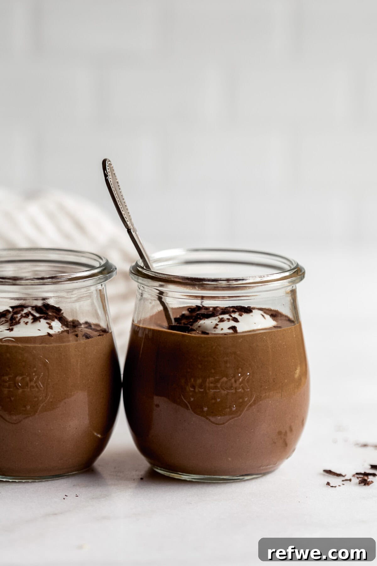 two cups of cottage cheese chocolate mousse in small jars on a marble countertop.