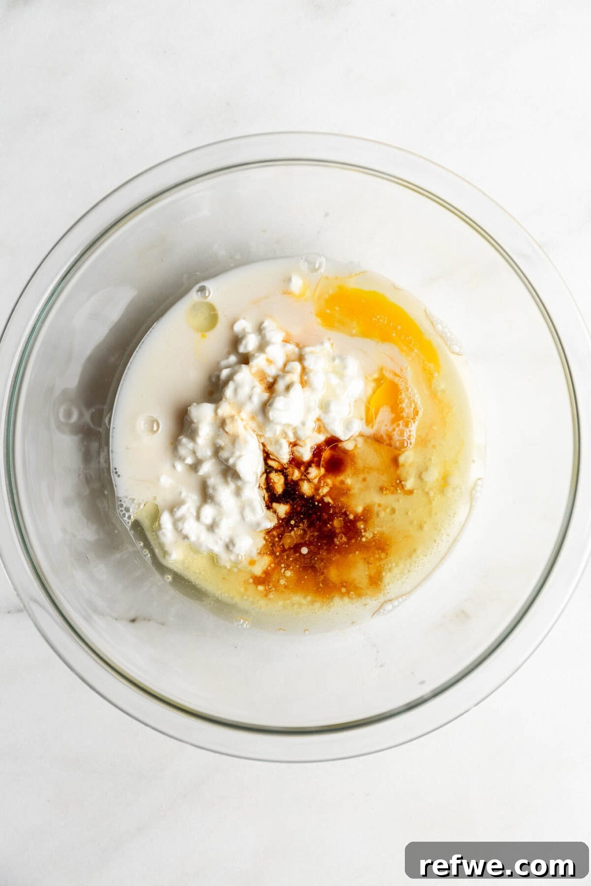 A large mixing bowl containing cottage cheese, milk, egg, oil, and vanilla extract.