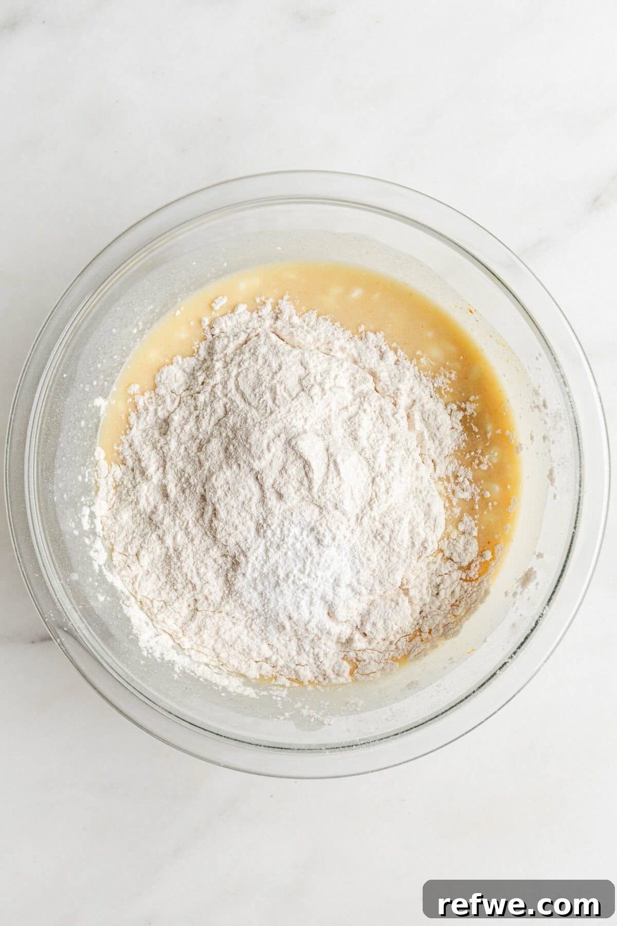 Dry ingredients, including flour, baking powder, baking soda, and salt, added to the wet mixture in a mixing bowl for blueberry muffins.