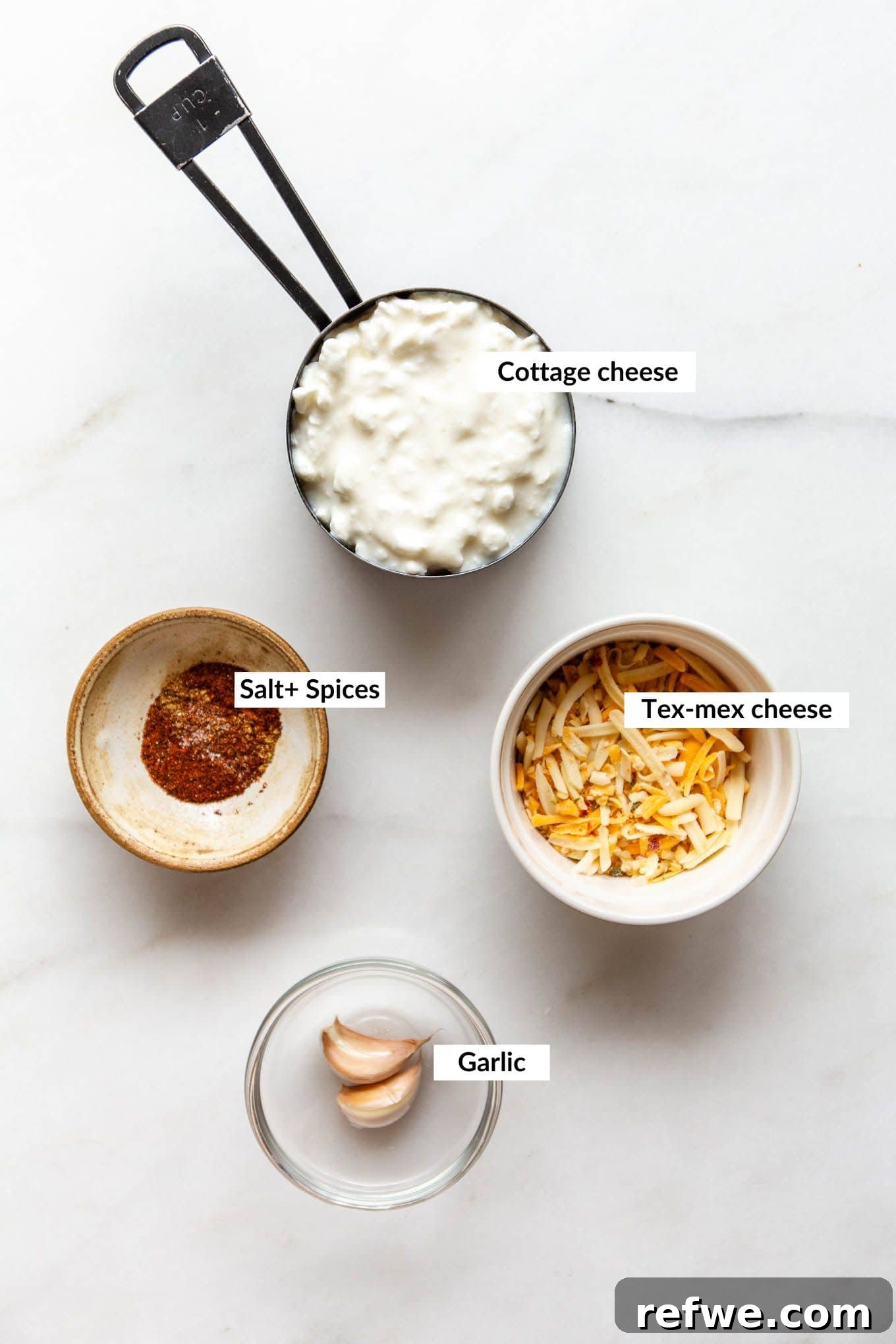Whipped Cottage Queso Dip 3 Individual ingredients neatly arranged, including cottage cheese, shredded Tex-Mex cheese, spices, and fresh garlic, ready for blending into queso.