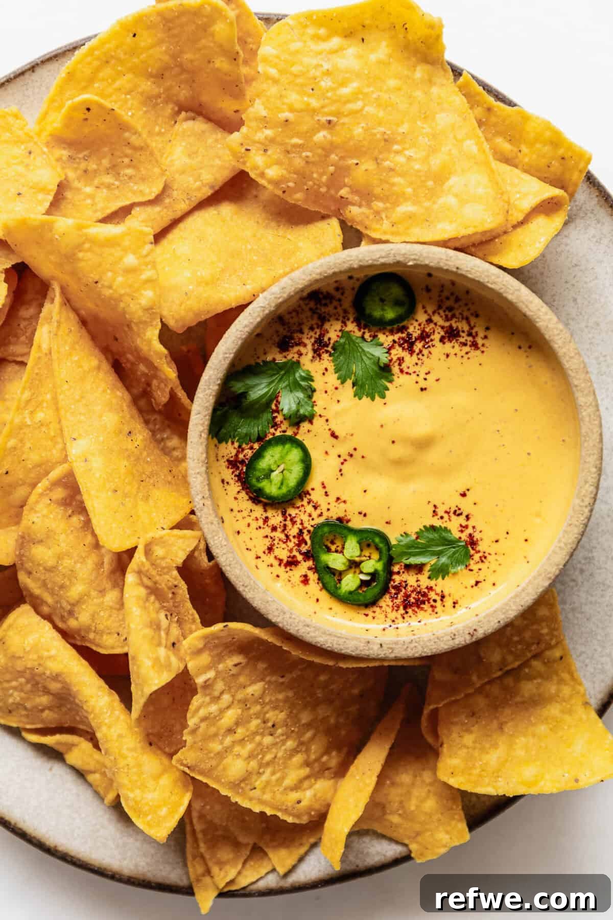 Whipped Cottage Queso Dip 7 A small, inviting bowl of cottage cheese queso dip, perfectly placed on a plate alongside a generous serving of crispy tortilla chips, creating an irresistible snack.