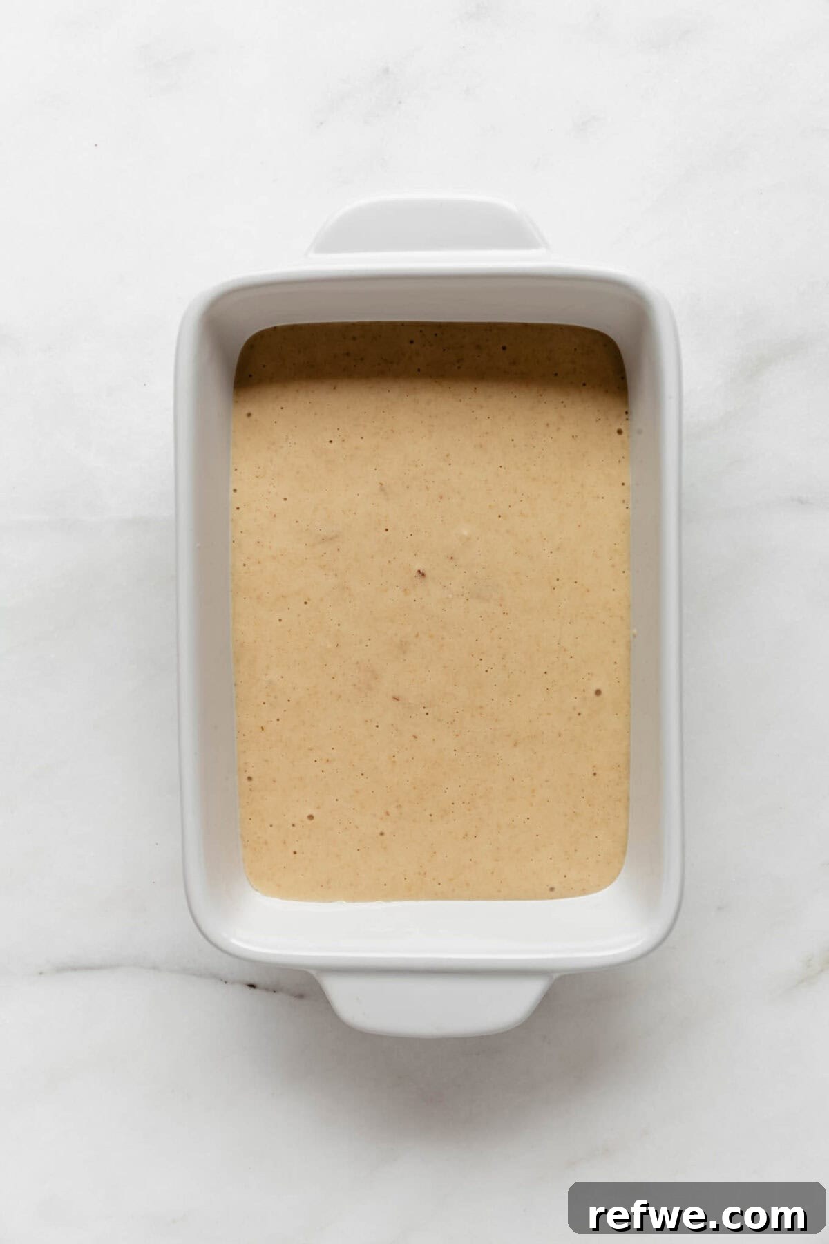 Peak Performance Pancake Bowl 6 The smoothly blended protein pancake bowl batter is carefully poured into a clean, white baking dish, ready for the oven.