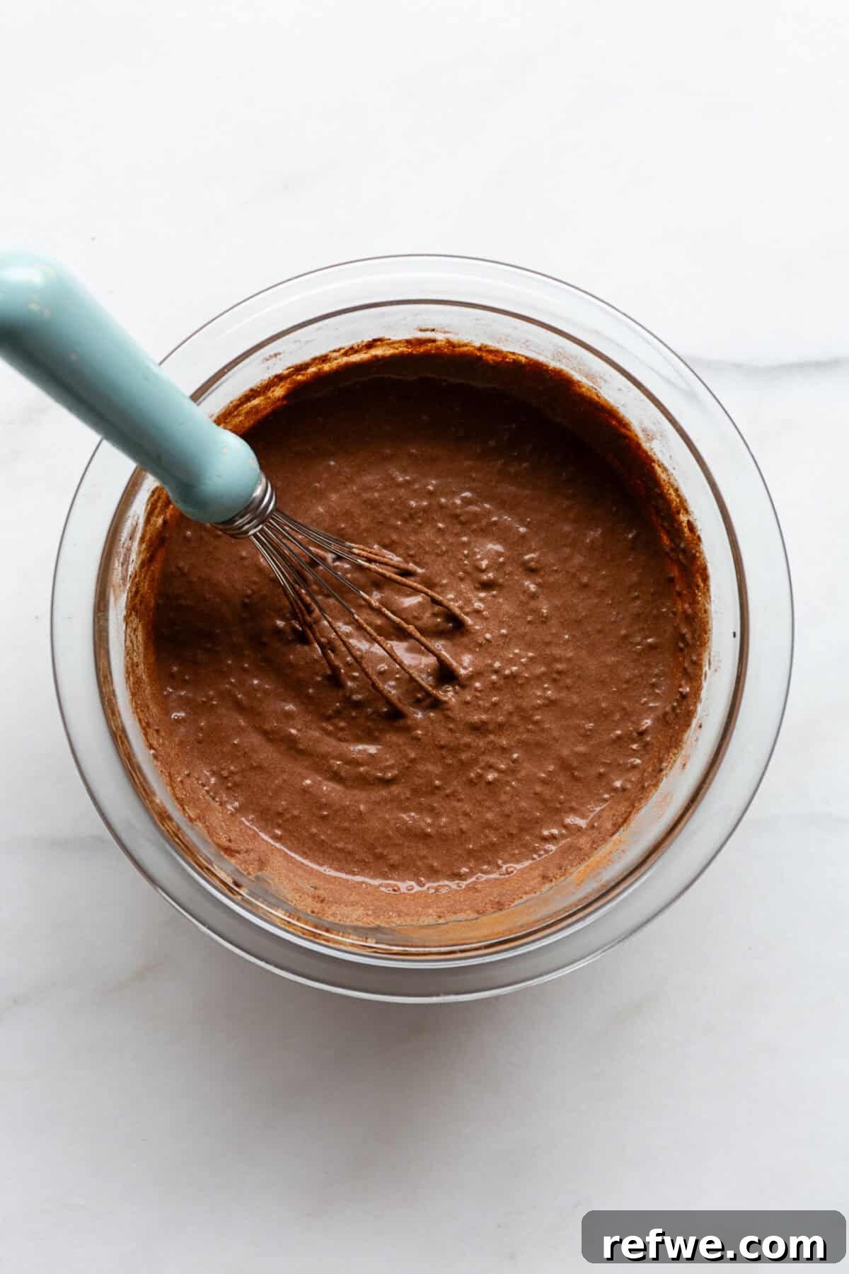 Peanut Butter Chocolate Chia Delight 5 un-set chocolate chia pudding in a mixing bowl with a blue whisk.