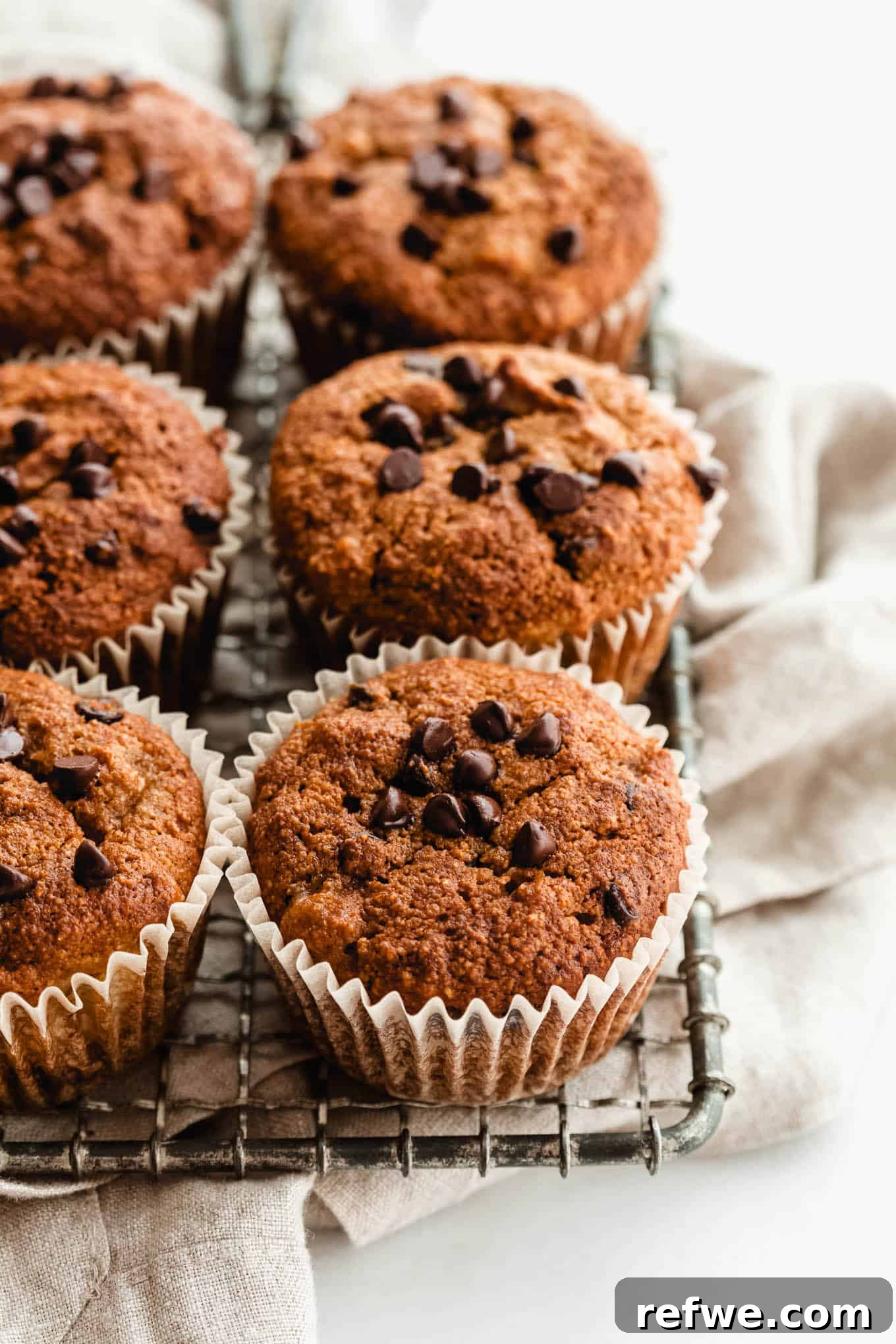 Wholesome Almond Banana Muffins 12 Two beautifully baked banana almond flour muffins resting on a cooling rack beside a beige napkin, showcasing their golden tops.