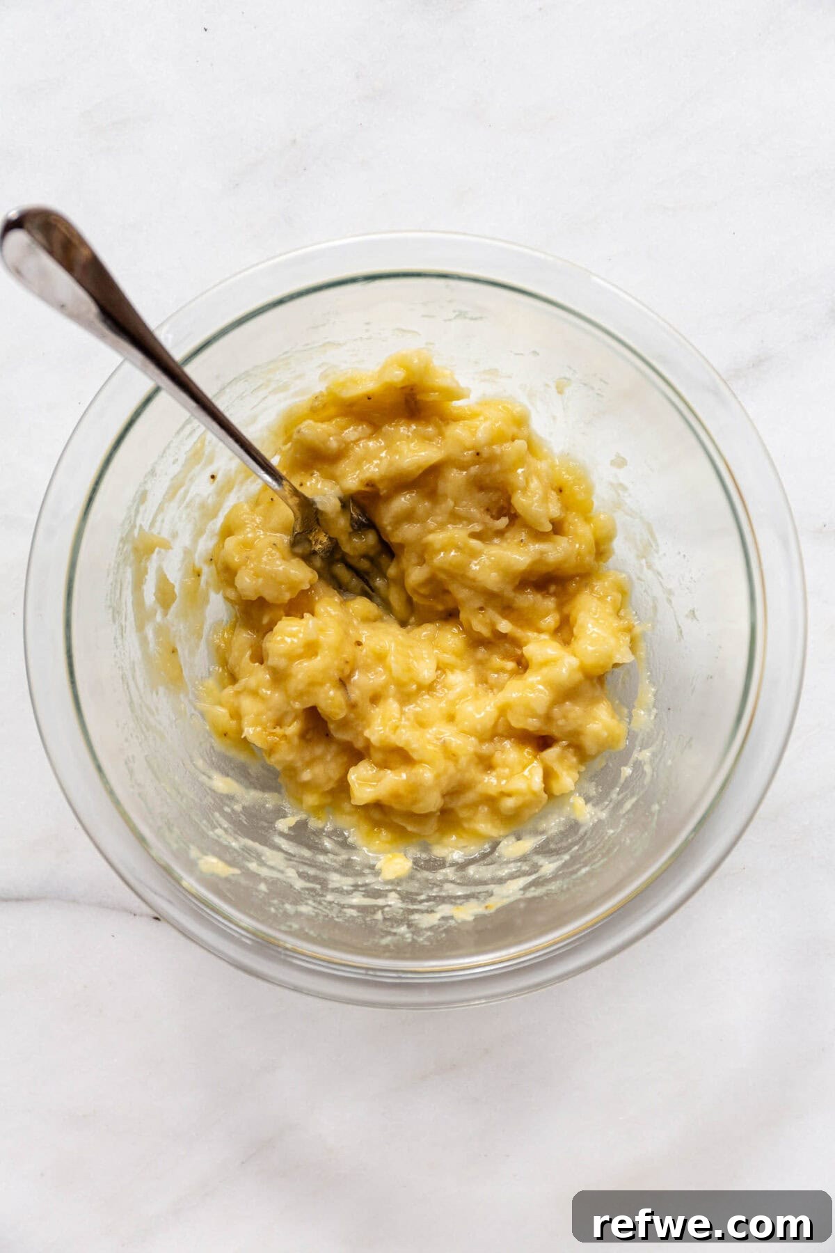 Wholesome Almond Banana Muffins 4 Mashed ripe bananas in a clear bowl with a fork, ready for mixing.