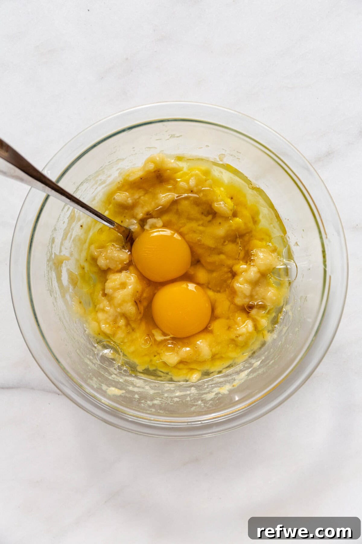 Wholesome Almond Banana Muffins 5 Mashed bananas mixed with two eggs in a clear bowl, creating a smooth wet mixture.