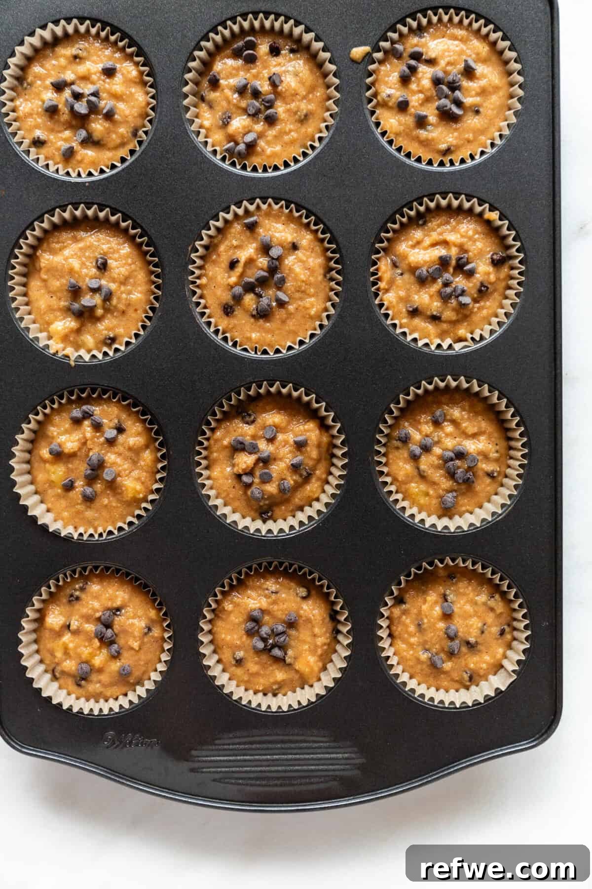 Wholesome Almond Banana Muffins 10 Unbaked banana almond flour muffin batter neatly spooned into a muffin pan lined with paper cups.
