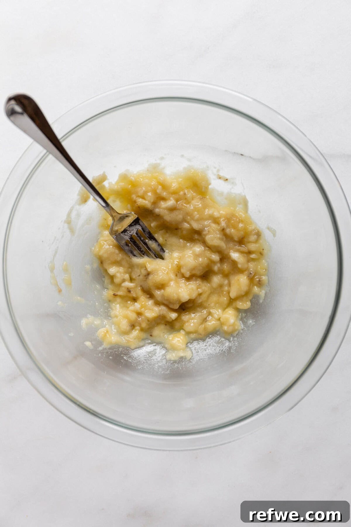 A bowl of mashed banana with a fork, ready for mixing.