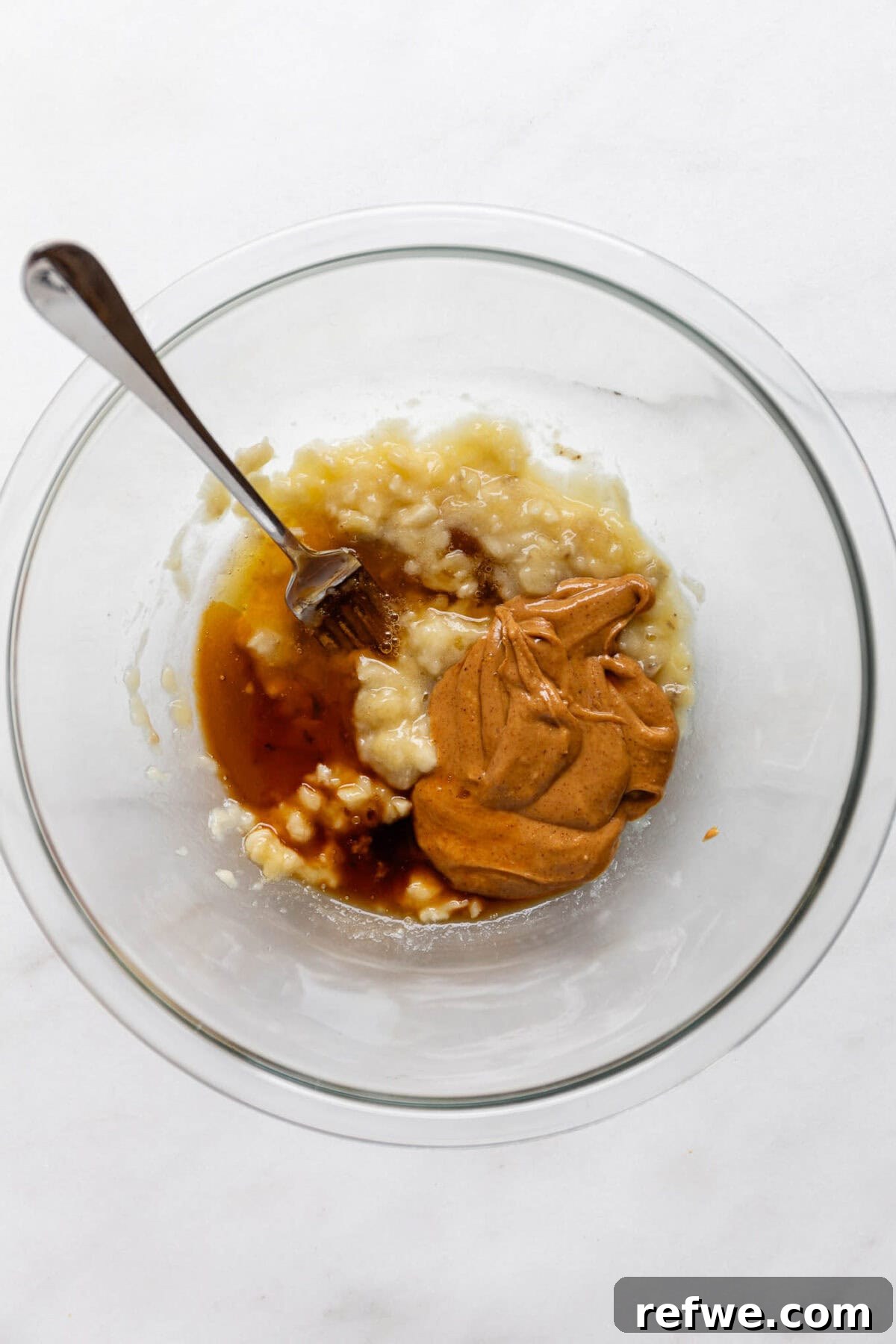Mashed banana, maple syrup, and peanut butter being combined in a bowl.