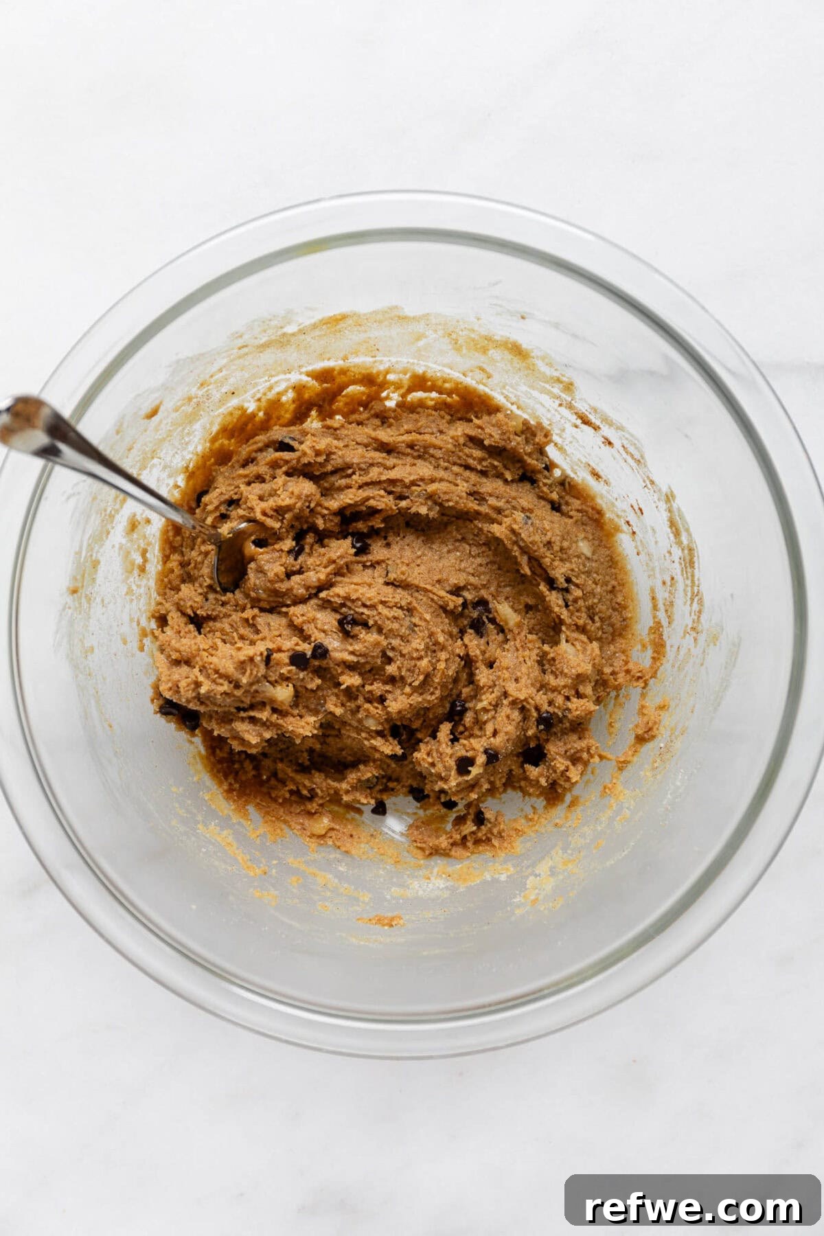 The banana protein ball dough fully mixed in a bowl with a spoon, showing a thick, cohesive texture.