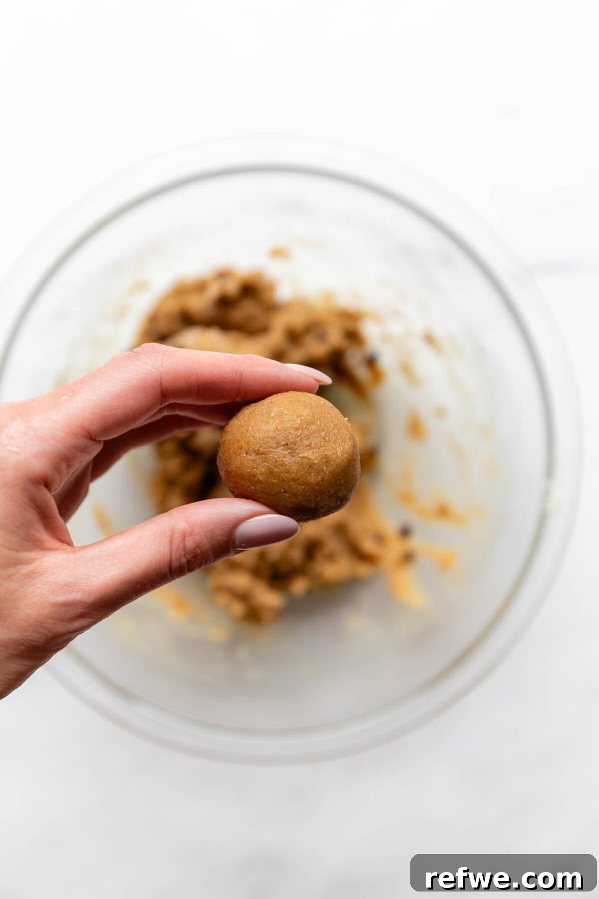 A hand holding a perfectly rolled banana protein ball, showcasing its even shape.