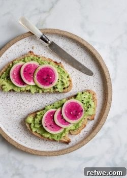 A crisp slice of sourdough toast generously topped with smashed avocado and decorative slices of watermelon radish, garnished with sesame seeds.