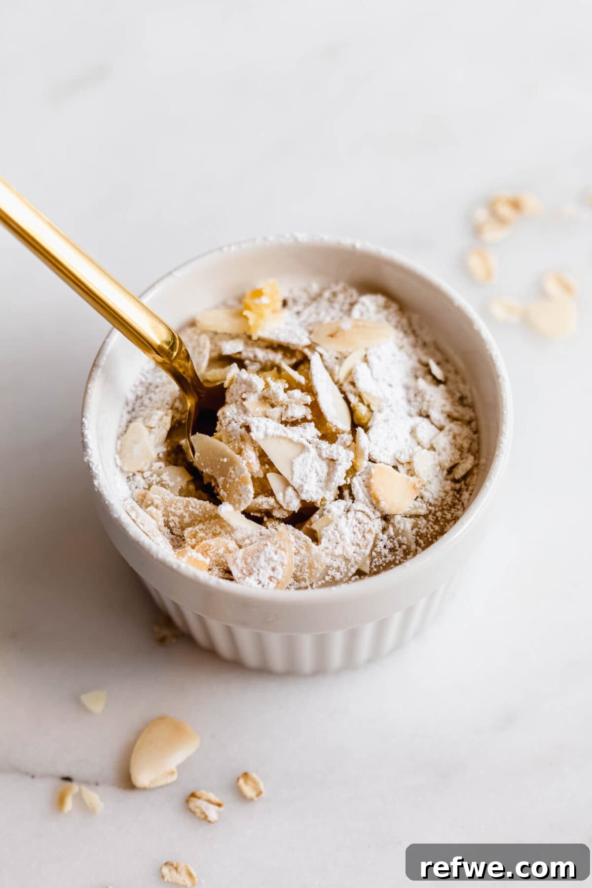 A gold spoon scooping almond baked oats out of a ramekin, with powdered sugar dusted on top.