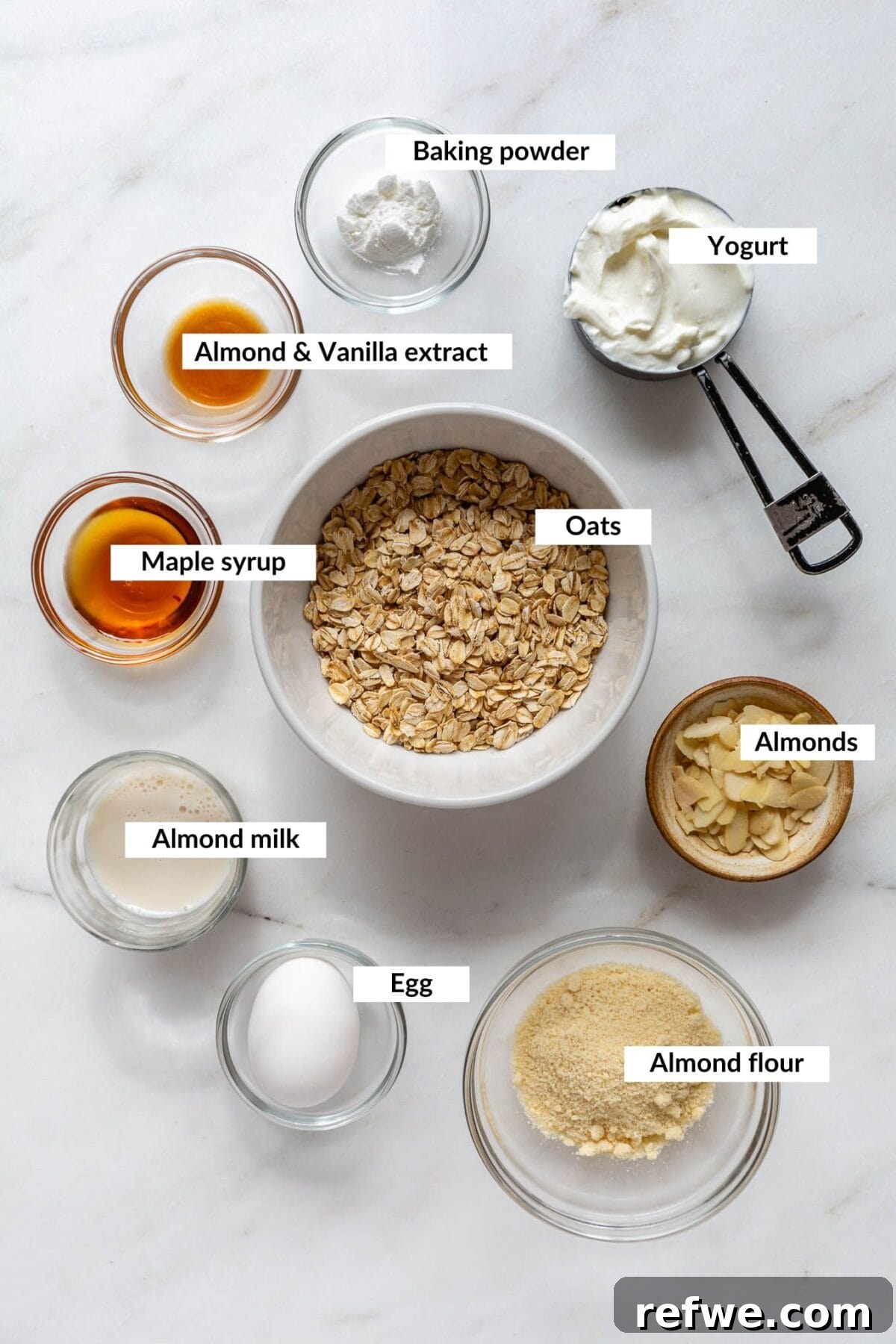 Key ingredients for almond croissant baked oats laid out on a wooden surface, including oats, almond extract, and yogurt.