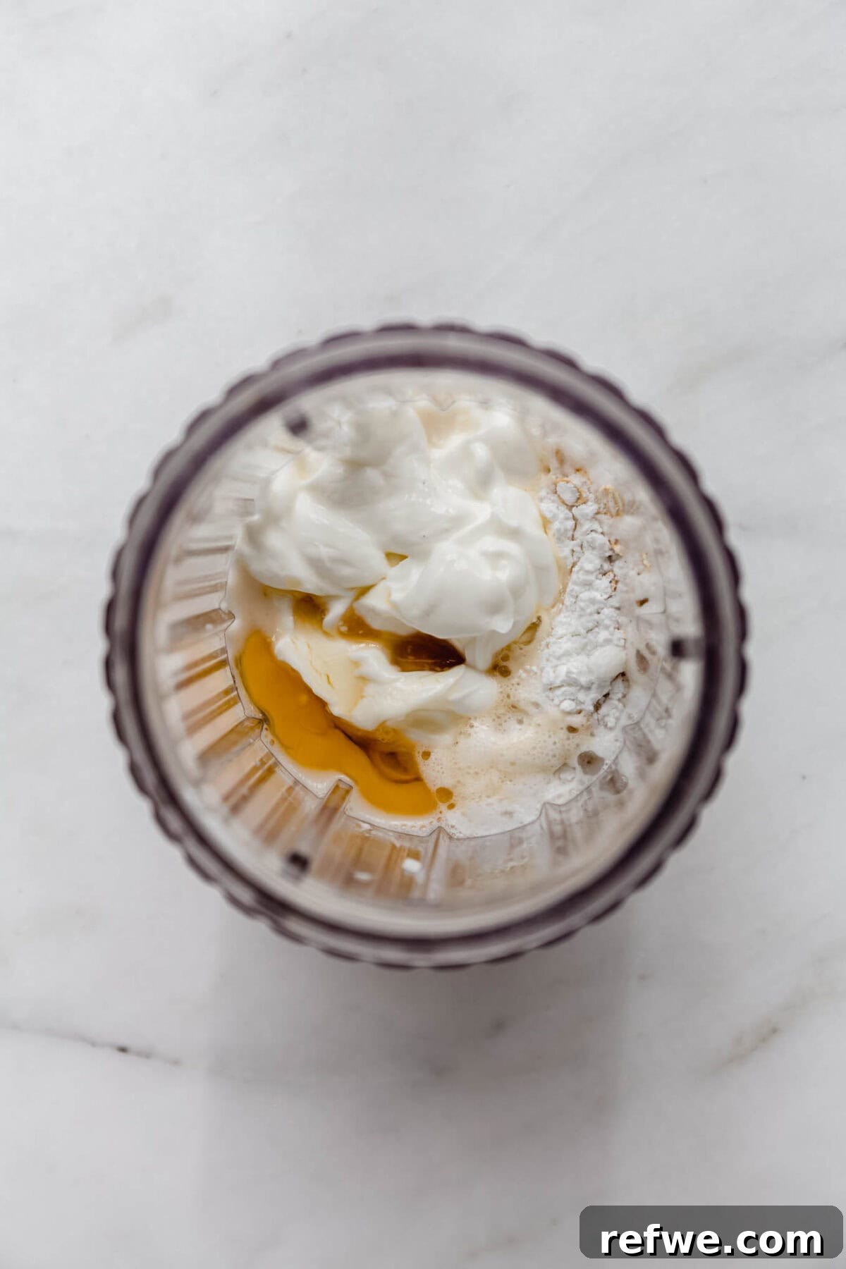 All baked oats ingredients, including oats, milk, yogurt, and extracts, being added to a blender.