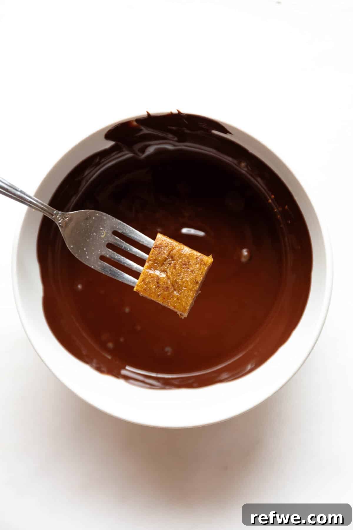 Date Caramel Chocolate Indulgence 8 A fork holding a date caramel square poised above a bowl of rich melted chocolate.