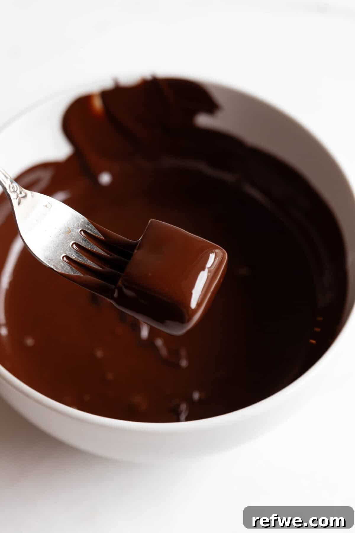 Date Caramel Chocolate Indulgence 9 A date caramel square perfectly dipped and coated in melted chocolate, held by a fork.