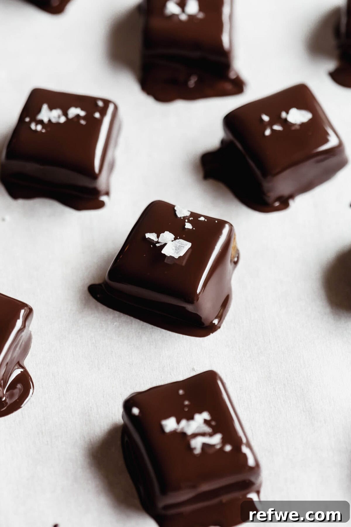 Date Caramel Chocolate Indulgence 10 Finished chocolate-dipped date caramels arranged on parchment paper, sprinkled with flaky sea salt.