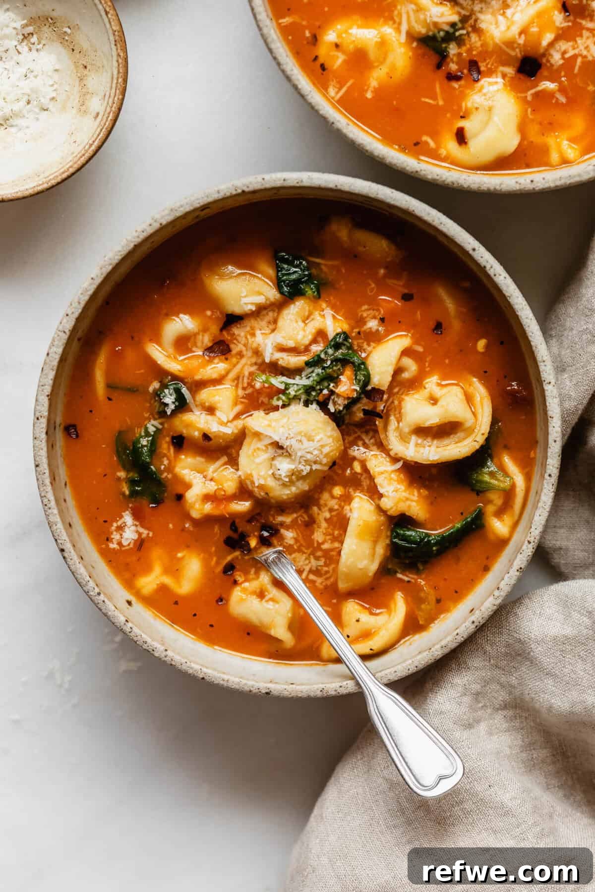 Velvety Tuscan Tortellini Soup 2 A bowl of creamy Tuscan tortellini soup, garnished with freshly grated Parmesan cheese and fresh basil leaves.
