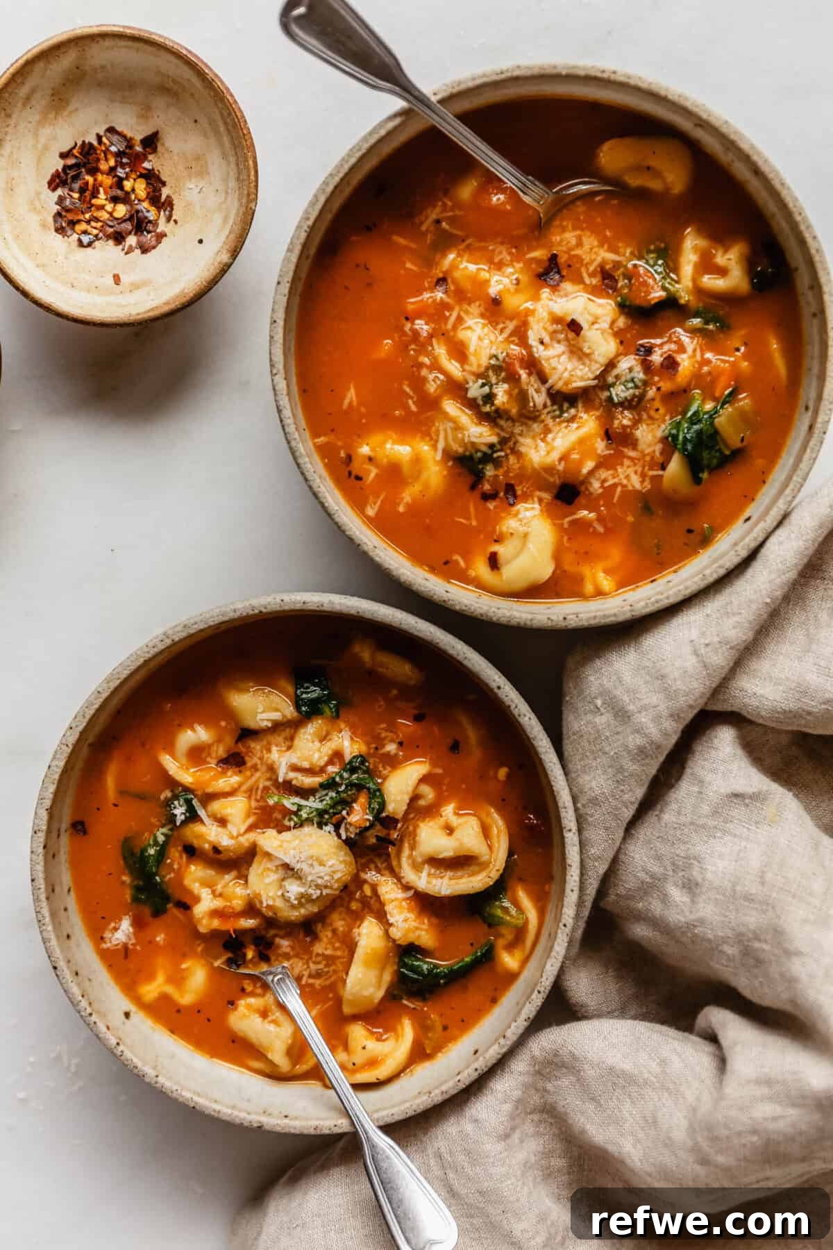Velvety Tuscan Tortellini Soup 12 Two cozy bowls of creamy Tuscan tortellini soup, served side-by-side on a rustic table with a folded beige napkin.