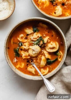 A bowl of tuscan tortellini soup with grated parmesan cheese on top.