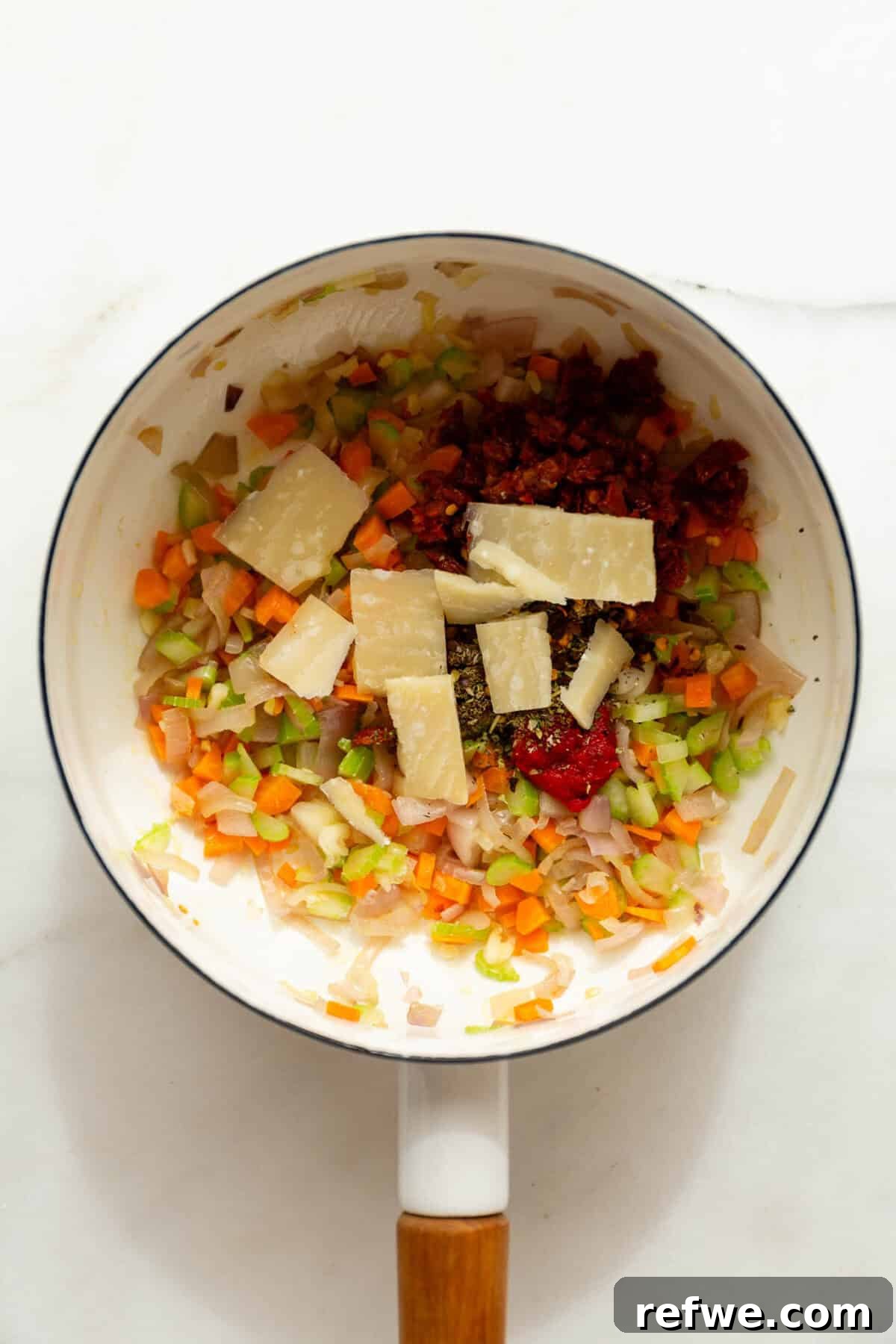 Velvety Tuscan Tortellini Soup 6 A mix of sautéed vegetables, sun-dried tomatoes, tomato paste, Italian seasoning, and a cube of Parmesan cheese in a white pot, ready for broth.