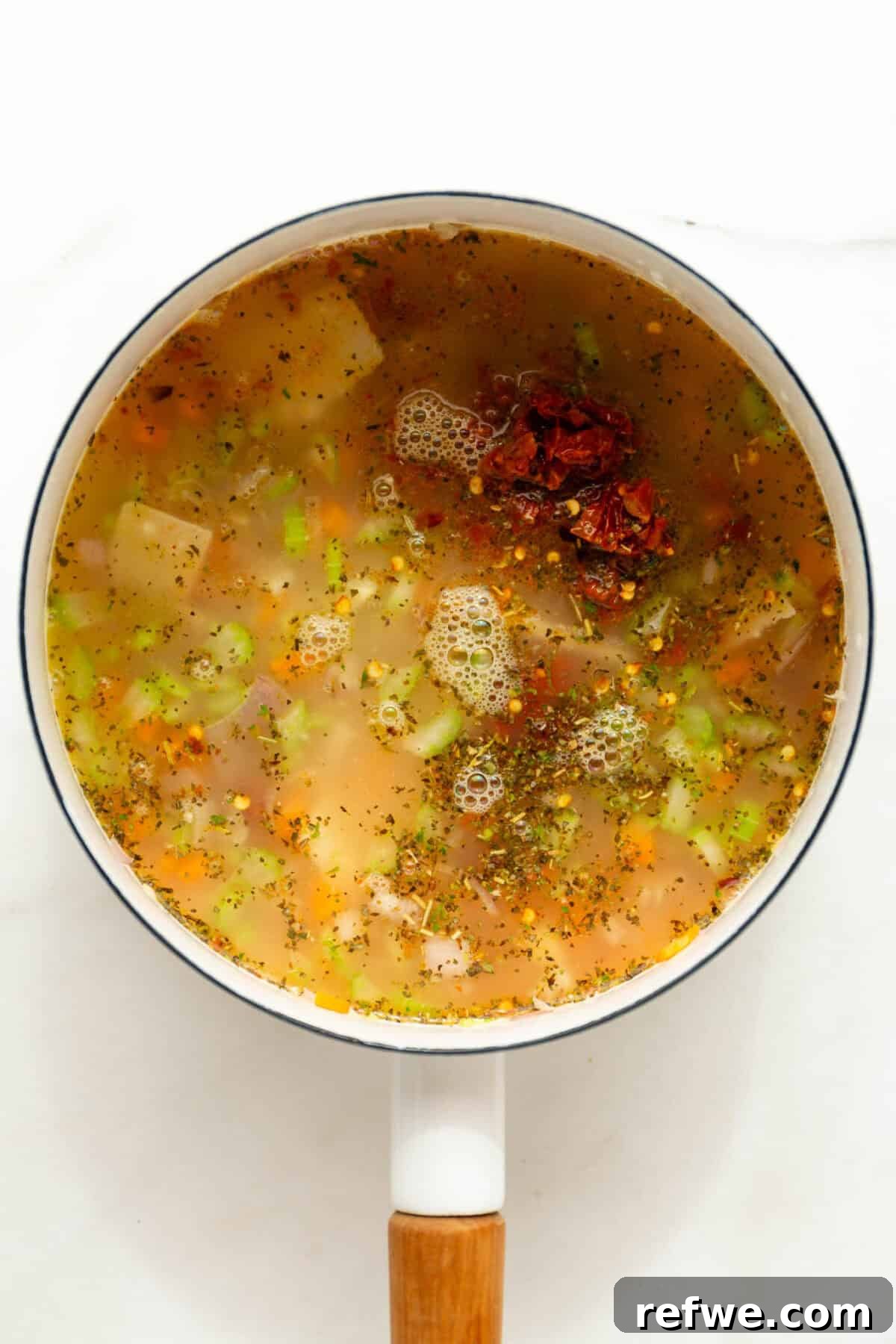 Velvety Tuscan Tortellini Soup 7 Rich, simmering Tuscan soup broth with vegetables and herbs in a white pot, covered and steaming.