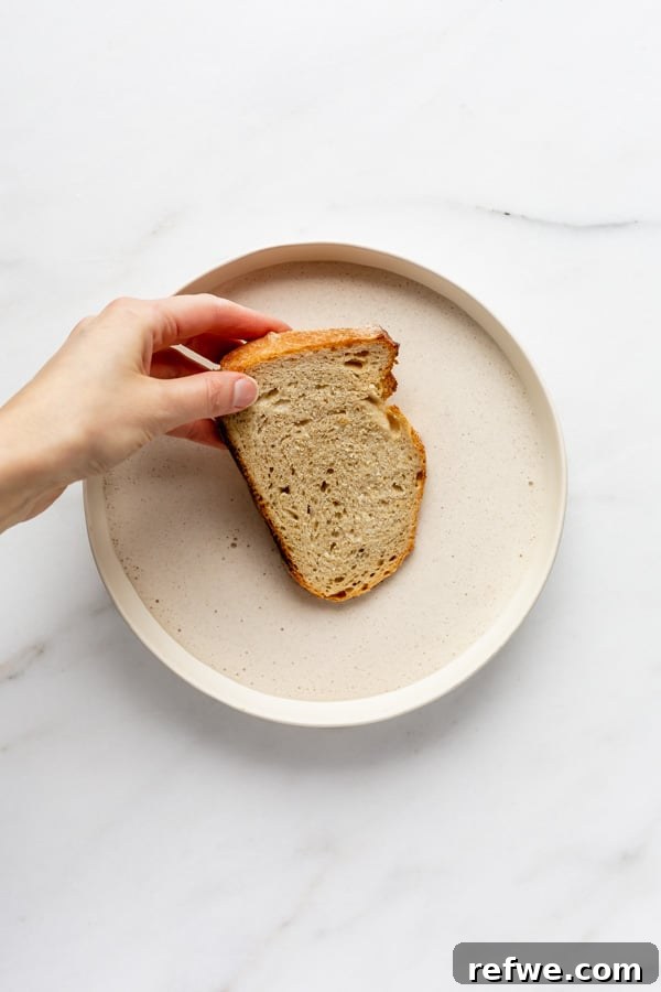 A piece of thick-cut bread being gently dipped into a bowl of vegan French toast batter.