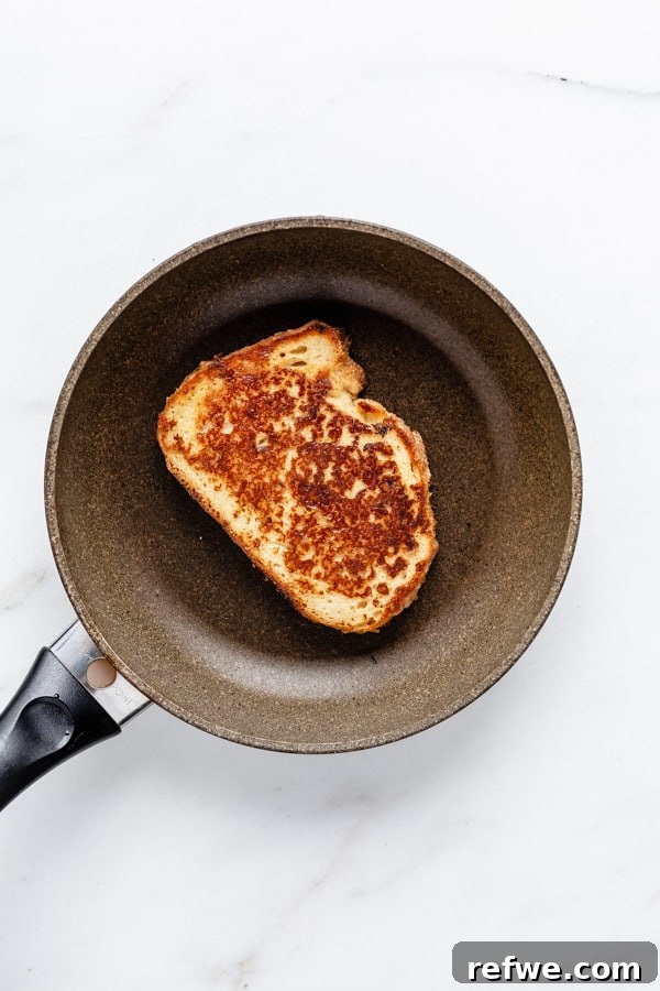 A single slice of vegan French toast cooking in a non-stick pan, turning golden brown.