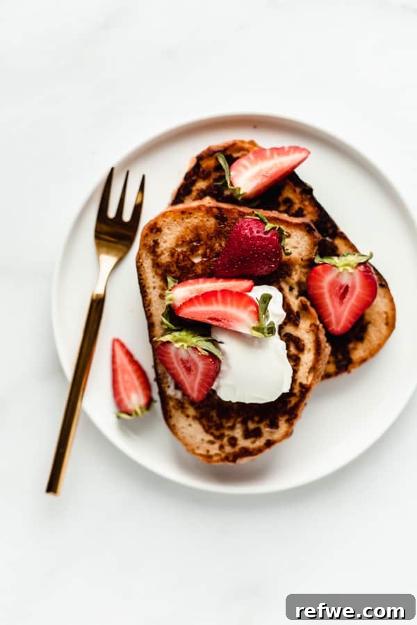 A beautifully plated stack of vegan French toast, garnished with fresh strawberries and powdered sugar.