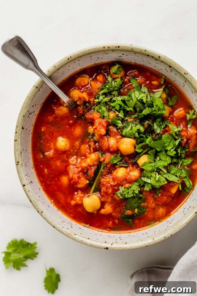 Fragrant Moroccan Chickpea Stew 2 Moroccan chickpea stew in a white speckled bowl, garnished with fresh cilantro, ready to be served.