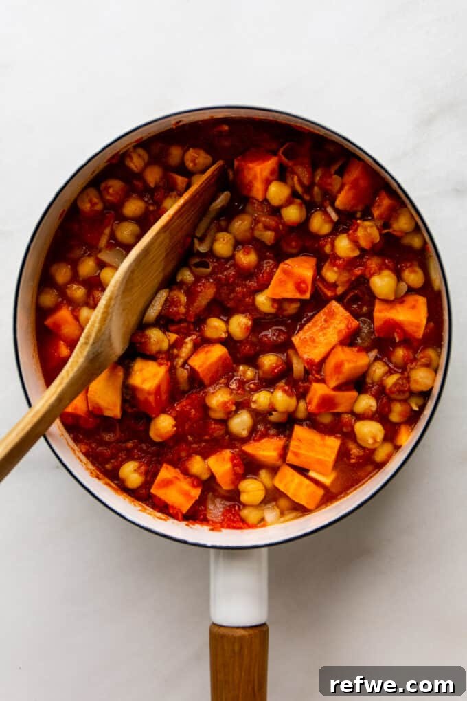 Fragrant Moroccan Chickpea Stew 6 A wooden spoon gently mixing the rich blend of potatoes, chickpeas, and tomato puree in a white pot.