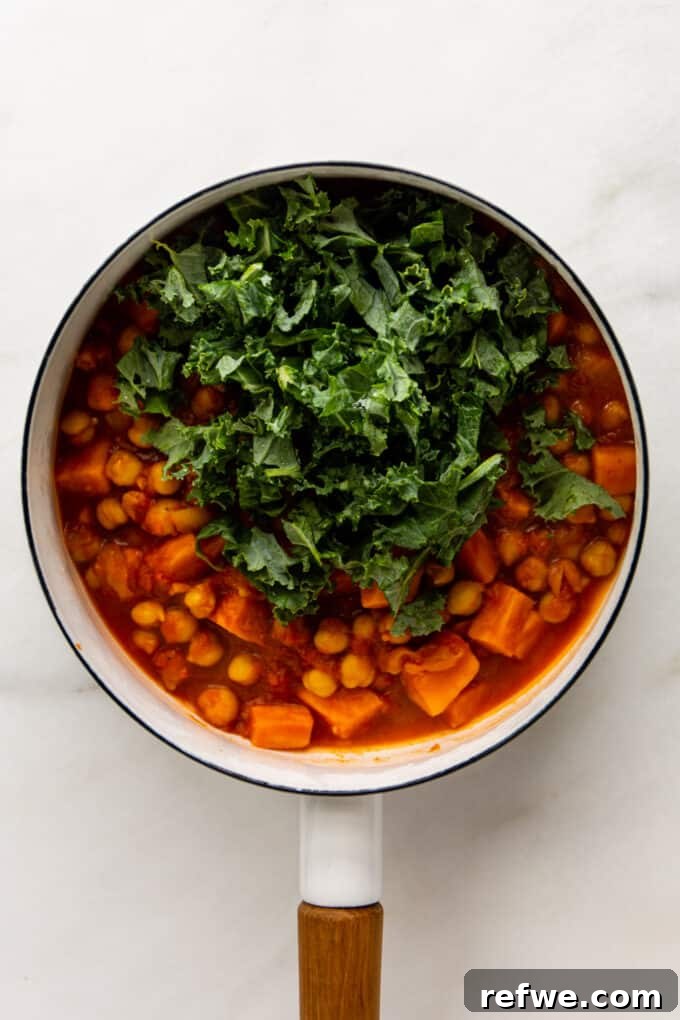 Fragrant Moroccan Chickpea Stew 7 Moroccan chickpea stew with freshly added kale, simmering in a large pot on the stove.