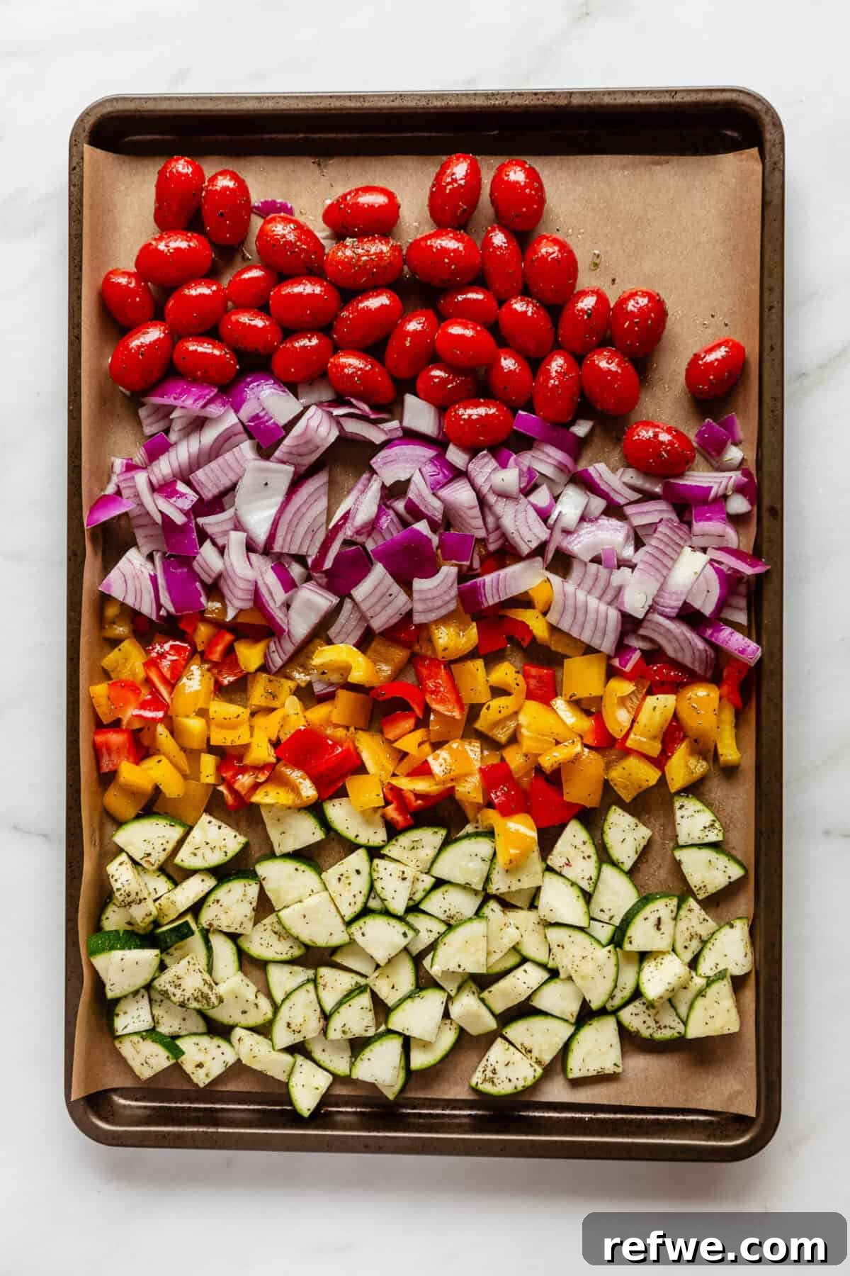 Vibrant Roasted Vegetable Quinoa Salad 4 Freshly chopped zucchini, bell peppers, cherry tomatoes, and red onion seasoned with Italian seasoning, olive oil, salt, and pepper on a parchment-lined baking sheet.