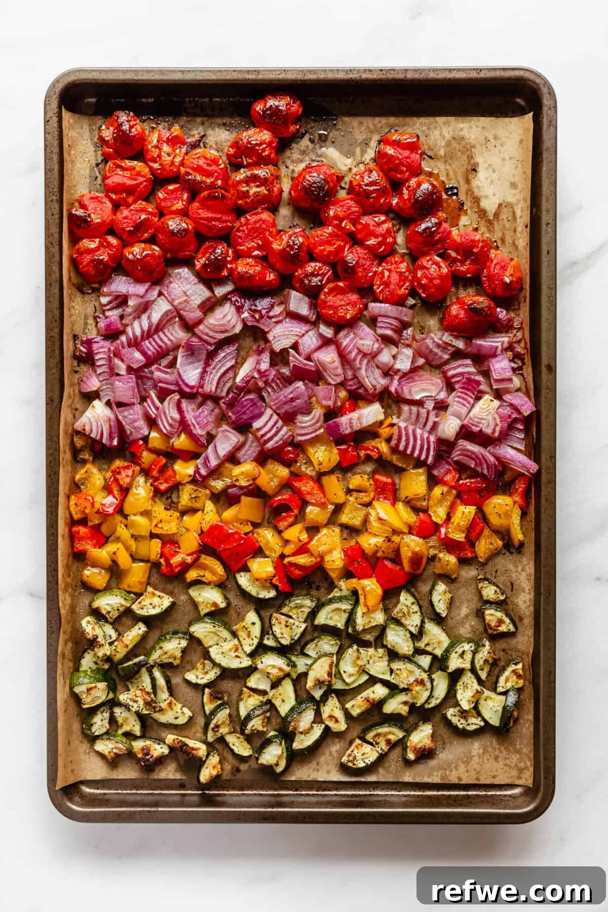 Vibrant Roasted Vegetable Quinoa Salad 5 Roasted vegetables including cherry tomatoes, zucchini, bell peppers, and red onion, beautifully caramelized and tender on a baking sheet.