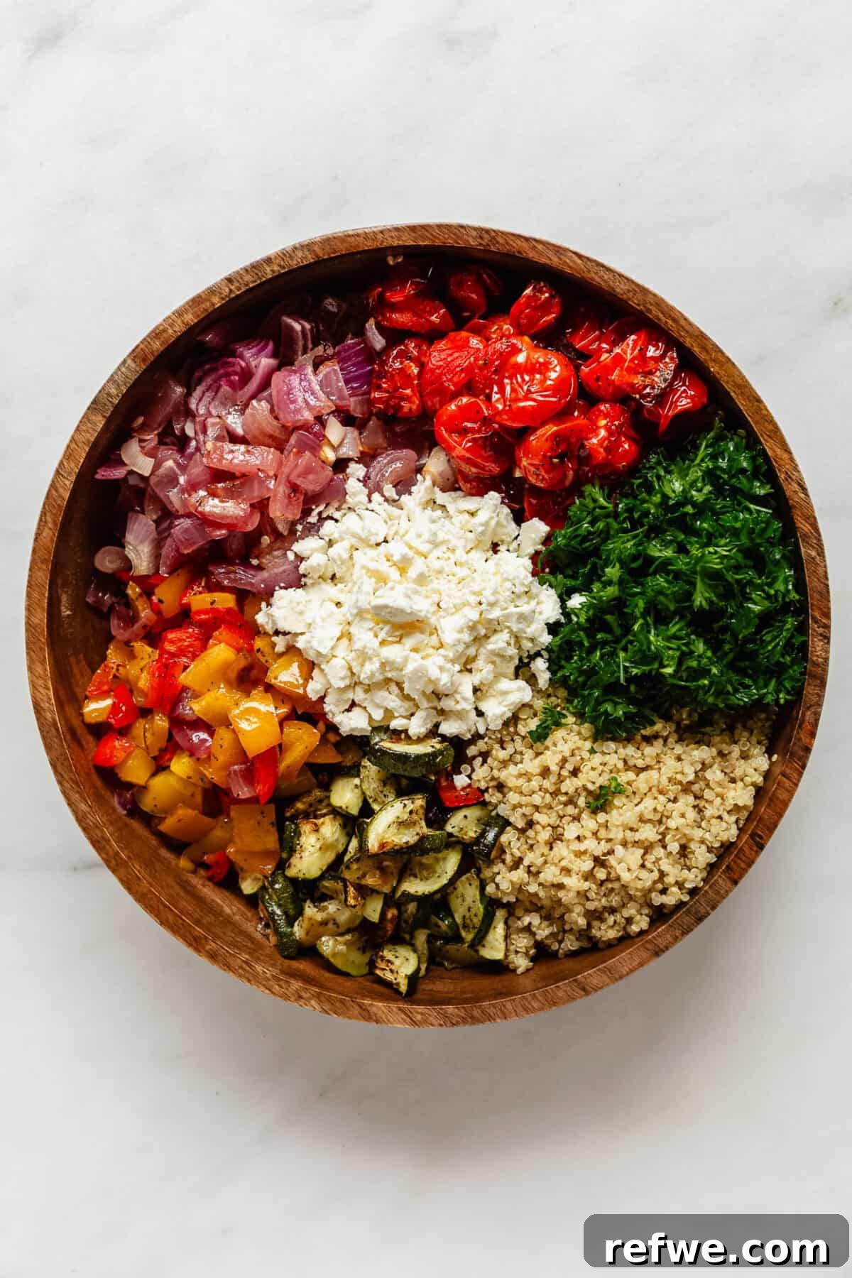 Vibrant Roasted Vegetable Quinoa Salad 6 A large wooden bowl filled with fluffy quinoa, freshly roasted vegetables, crumbled feta cheese, and chopped parsley, waiting to be tossed.