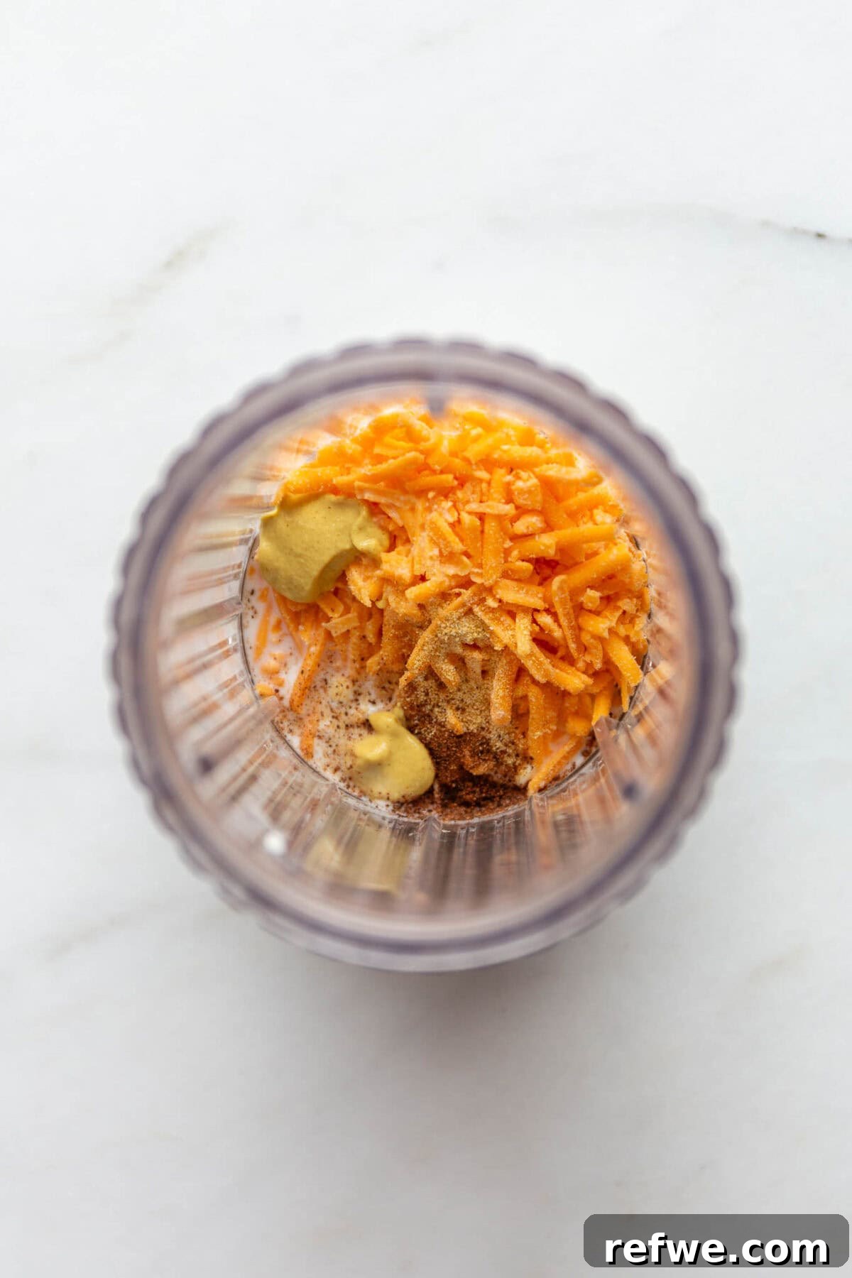 15-Minute Cottage Cheese Mac & Cheese Delight 4 Cottage cheese, shredded cheddar cheese, and a dollop of Dijon mustard in a blender container, ready for blending.