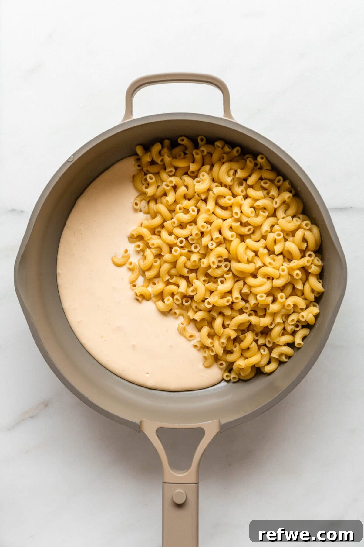 15-Minute Cottage Cheese Mac & Cheese Delight 6 Al dente macaroni noodles being combined with the freshly blended cottage cheese sauce in a taupe pan over medium heat.
