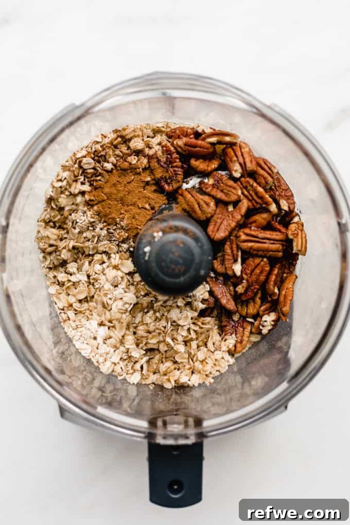 Guilt-Free Mini Pecan Treats 3 A food processor filled with the raw ingredients for the pecan pie crust, including whole oats, pecans, and a sprinkle of cinnamon, ready for blending.