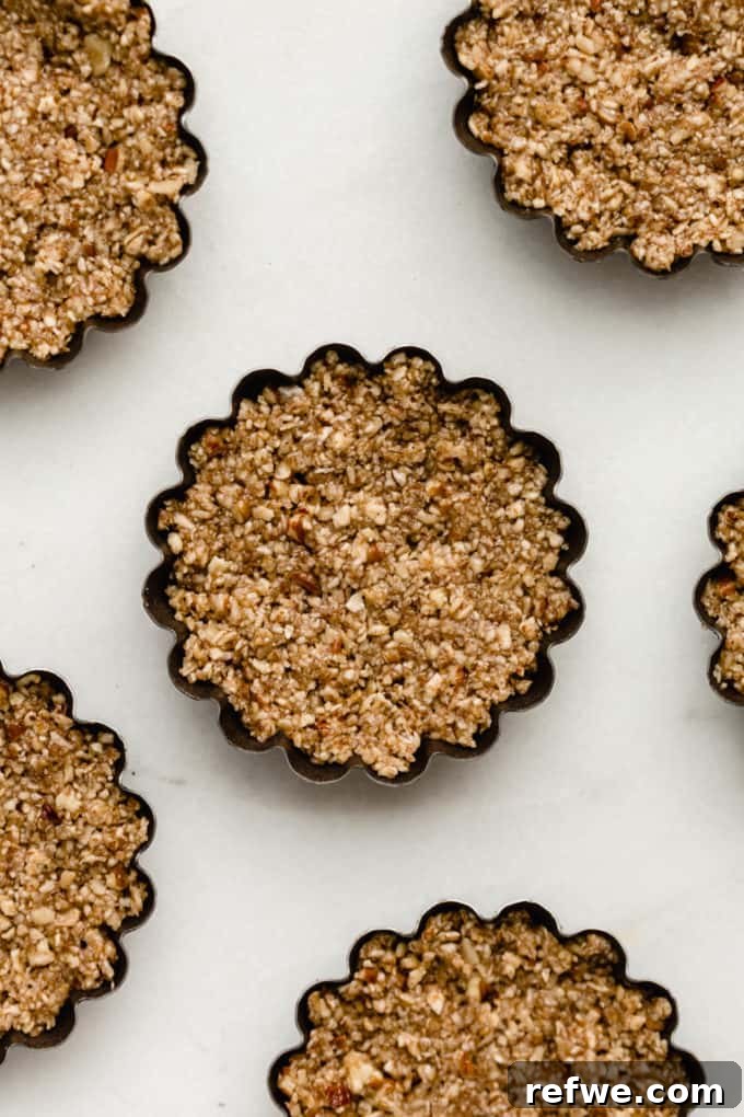 Guilt-Free Mini Pecan Treats 5 Close-up shot of several mini tart pans, each filled with the pressed pecan pie crust, ready to be baked to a golden perfection.