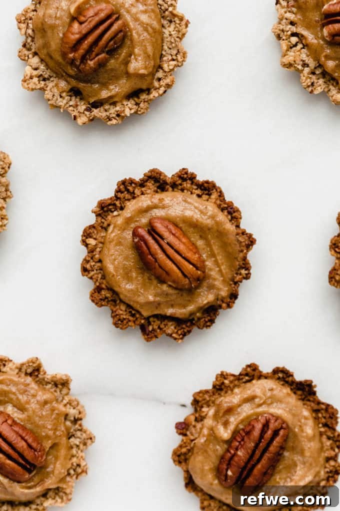 Guilt-Free Mini Pecan Treats 6 A perfectly assembled mini pecan pie, showcasing the golden baked crust generously topped with rich, creamy date caramel and finished with a whole pecan.