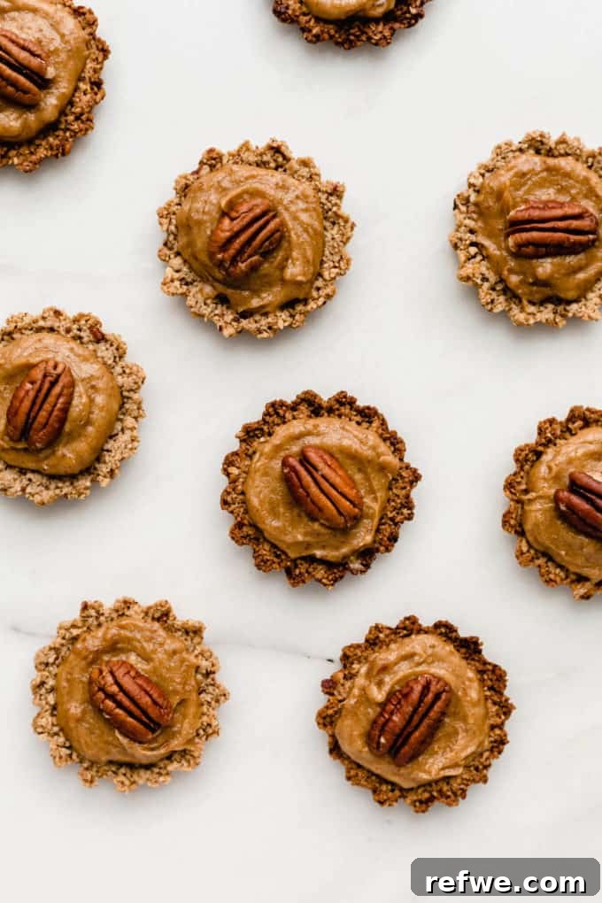 Guilt-Free Mini Pecan Treats 7 A stunning arrangement of healthy mini pecan pies, each perfectly topped with a pecan, presented on an elegant white marble board. These bite-sized desserts are ready to be served.
