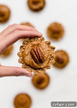 A hand holding up a mini pecan pie, featuring a golden crust and a rich, nutty filling.